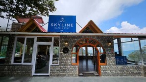 Edificio SKYLINE cafe & stay con fachada de piedra, ventanas grandes y vista a la montaña.