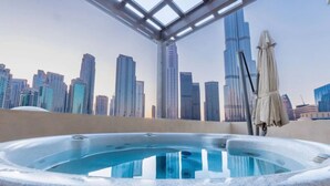 Un jacuzzi en la azotea con vistas a un horizonte urbano, una pérgola y una sombrilla.