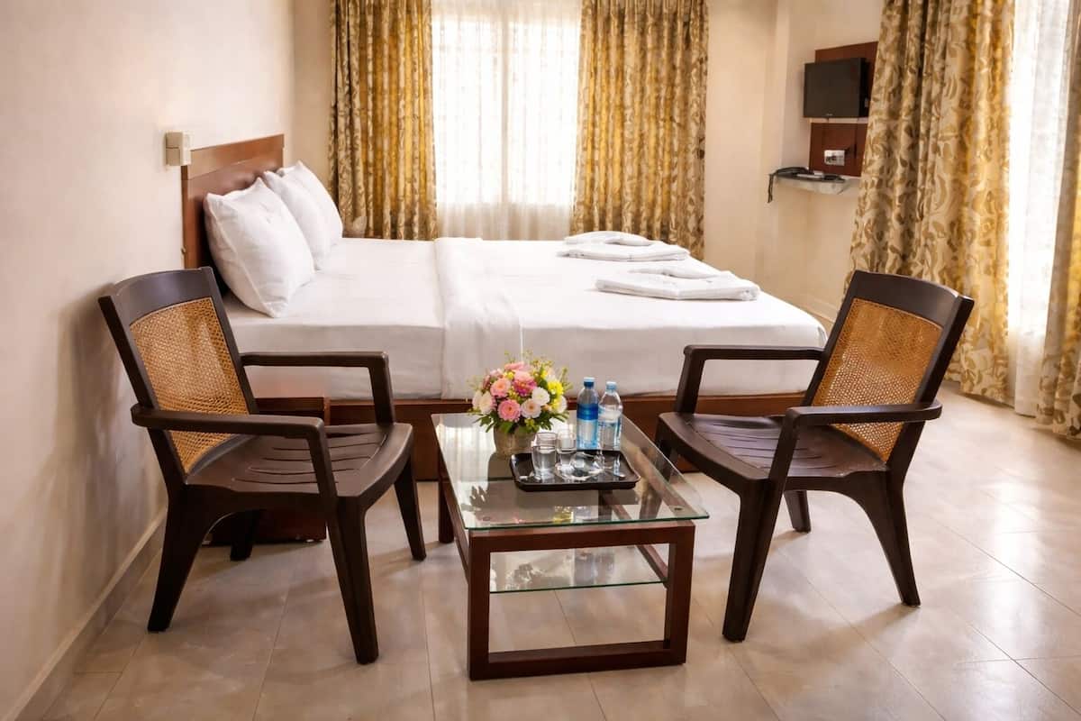 A hotel room with a bed, two chairs, a coffee table with water bottles, and a TV on the wall.
