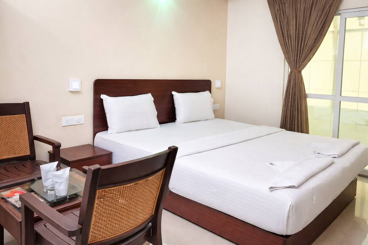 A hotel room with a large bed, a desk with a chair, and a window with curtains.