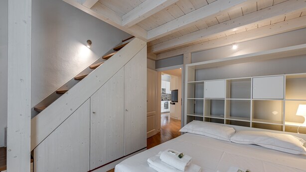 A bedroom with a wooden staircase, a bed with neatly folded white towels, and a white headboard with built-in lighting.
