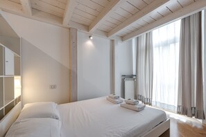 Quarto com cama, mesa de cabeceira, espelho, janela com cortinas e teto de madeira.