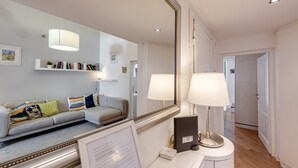A modern hotel room with a sofa, a bedside table with a lamp, a mirror, and a framed menu.