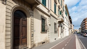 A street view with a building featuring a large wooden door and a window with a metal grille.
