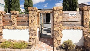 A stone wall with a wooden gate, a number sign, and a pathway leading to a building. - Main Home & Guest House | Dining On The Patio! (San Diego)