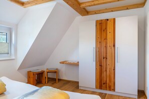 Ein Schlafzimmer mit schrägen Wänden, einem Holzschrank, einem Bett, zwei Hocker und einem kleinen Tisch.