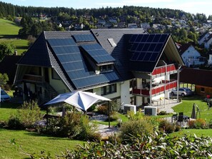 Une maison moderne dotée de panneaux solaires sur le toit, d’un espace de détente extérieur abrité et offrant une vue sur un quartier résidentiel.