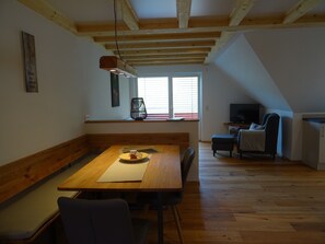 A dining area with a wooden table, benches, and a TV in the background.