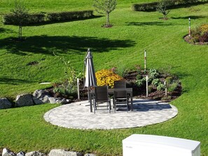 Une terrasse circulaire avec une table et des chaises, entourée d’une pelouse et d’un jardin bien entretenus.