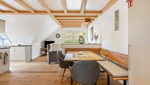 Une cuisine moderne avec des poutres en bois, un coin repas avec un banc et une vue sur l’extérieur.