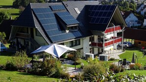 Une maison moderne dotée de panneaux solaires sur le toit, d’un espace de détente extérieur abrité et offrant une vue sur un quartier résidentiel.