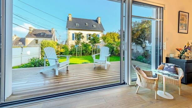 Een modern interieur met een schuifdeur die leidt naar een terras, rieten meubels en een lijst met een afbeelding aan de muur.