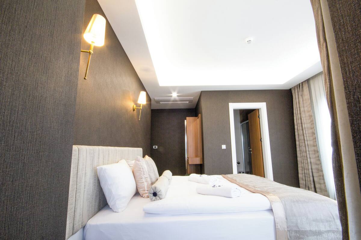 A modern hotel room with a neatly made bed, a wall-mounted lamp, and a door leading to another room.