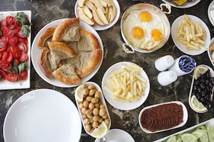 Variedad de alimentos como pan, huevos, tomates y aceitunas, todo dispuesto sobre una superficie de mármol.