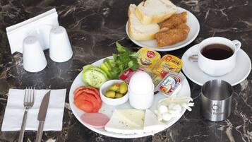 Una mesa de desayuno con un plato de comida, que incluye pan, huevos, queso y verduras, además de salsas y una taza de café.