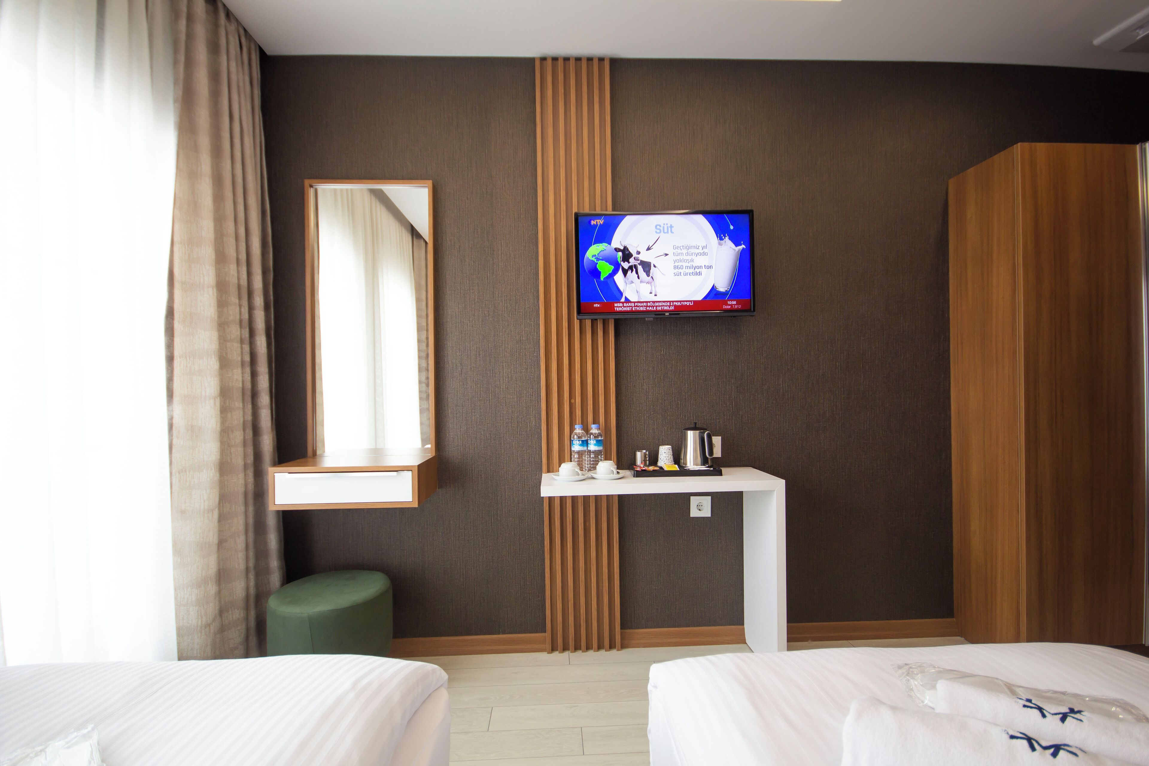 A hotel room with two beds, a television mounted on the wall, a small table with a kettle, and a mirror.
