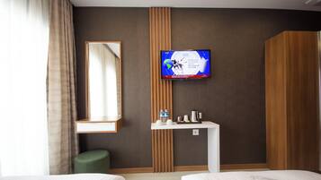 A hotel room with two beds, a television mounted on the wall, a small table with a kettle, and a mirror.