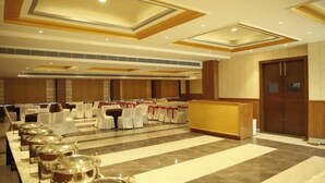 A banquet hall with a long table set for a meal, chairs with white covers, and a reception desk. - Hotel A9 Resorts (Raikot)