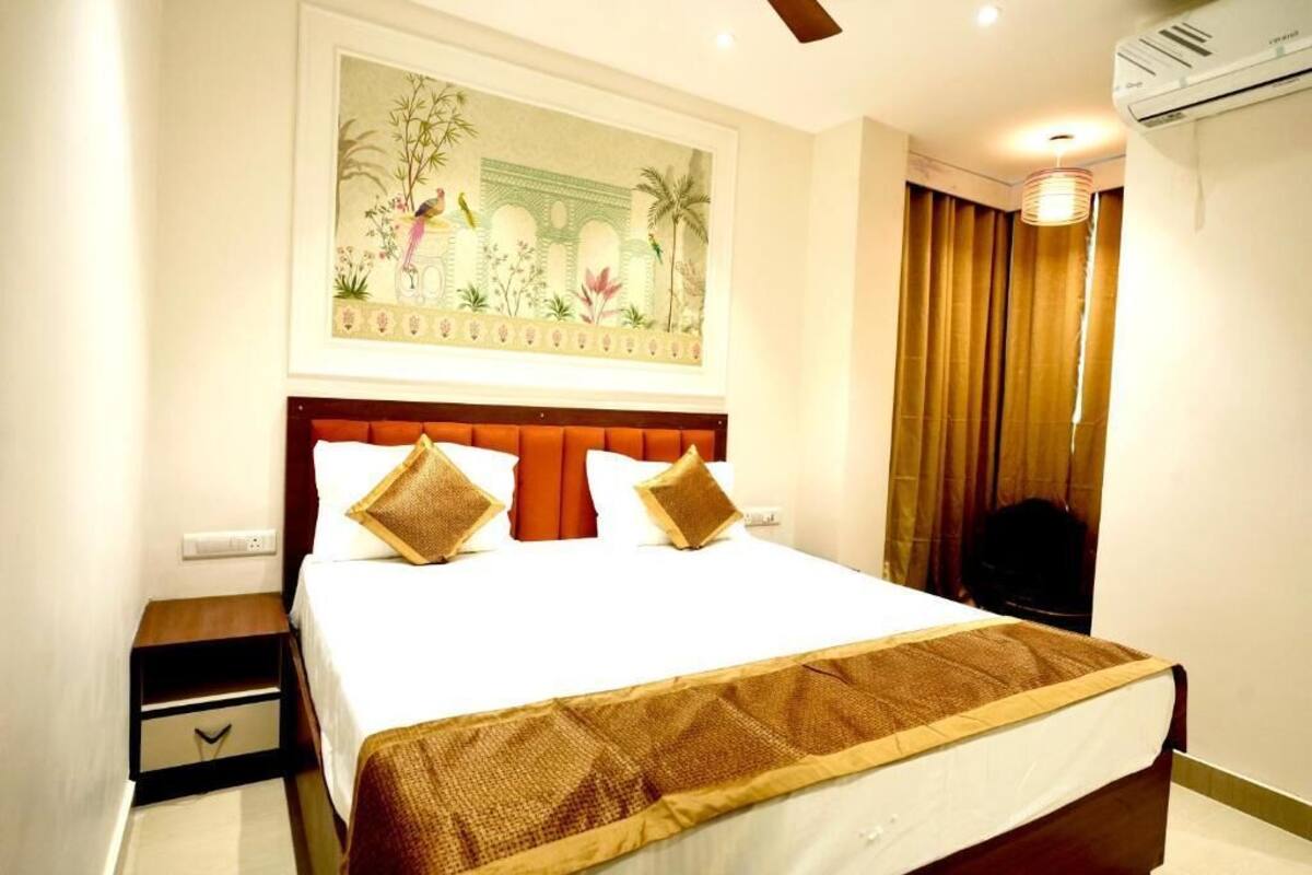 A hotel room with a large bed, a nightstand, a wall-mounted air conditioner, and a window with curtains.