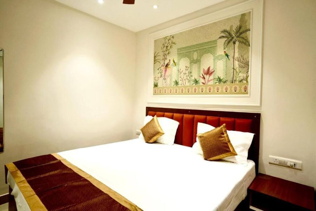 A hotel room with a large bed, a red headboard, and a wall-mounted painting of a garden scene.