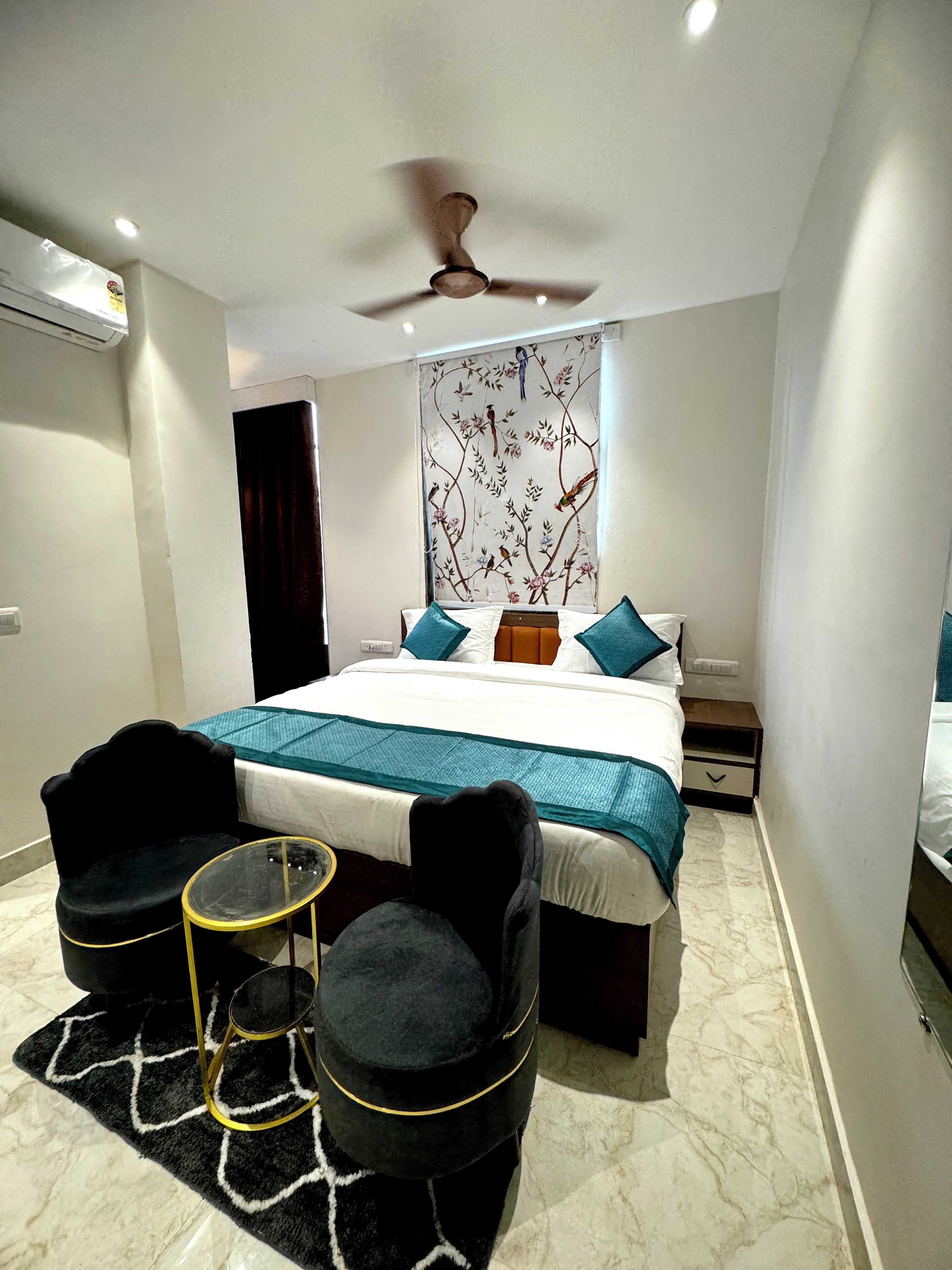 A modern bedroom with a large bed, two black chairs, a small round table, and a ceiling fan.
