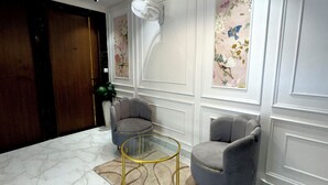A modern lobby with marble flooring, two grey armchairs, a glass coffee table, and decorative wall panels. - Ace Stayz (Varanasi)