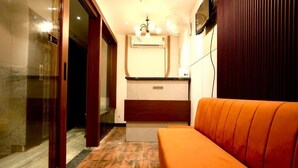 A hotel reception area with a reception desk, a sofa, and a wall-mounted TV. - Ace Stayz (Varanasi)