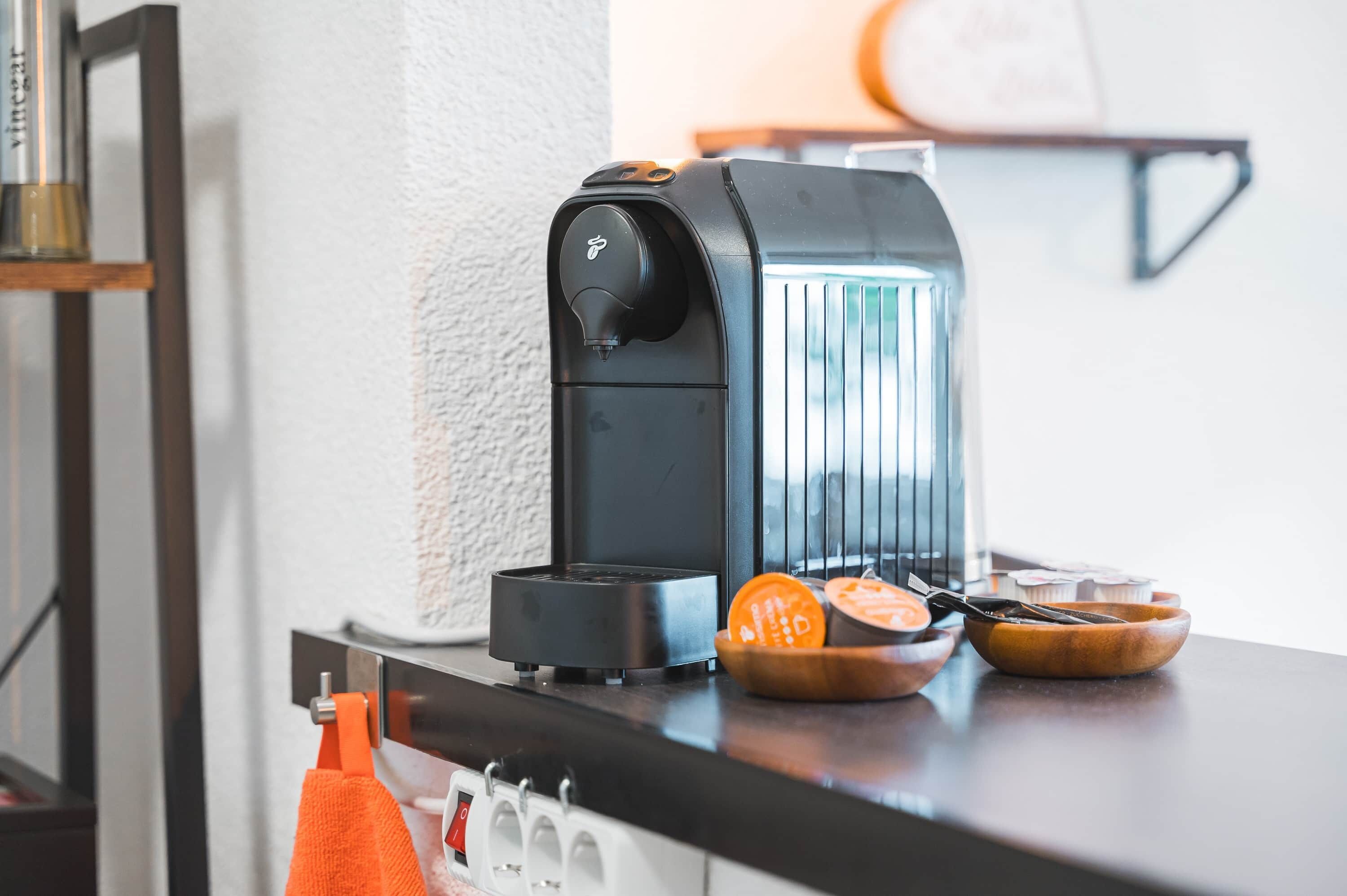 A kitchen with a coffee maker, a bowl of fruit, and a wooden cutting board.
