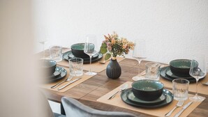 Ein Esstisch, gedeckt mit grünen Tellern, Schüsseln und klaren Gläsern, ergänzt durch eine Blumenvase und eine Kerze.