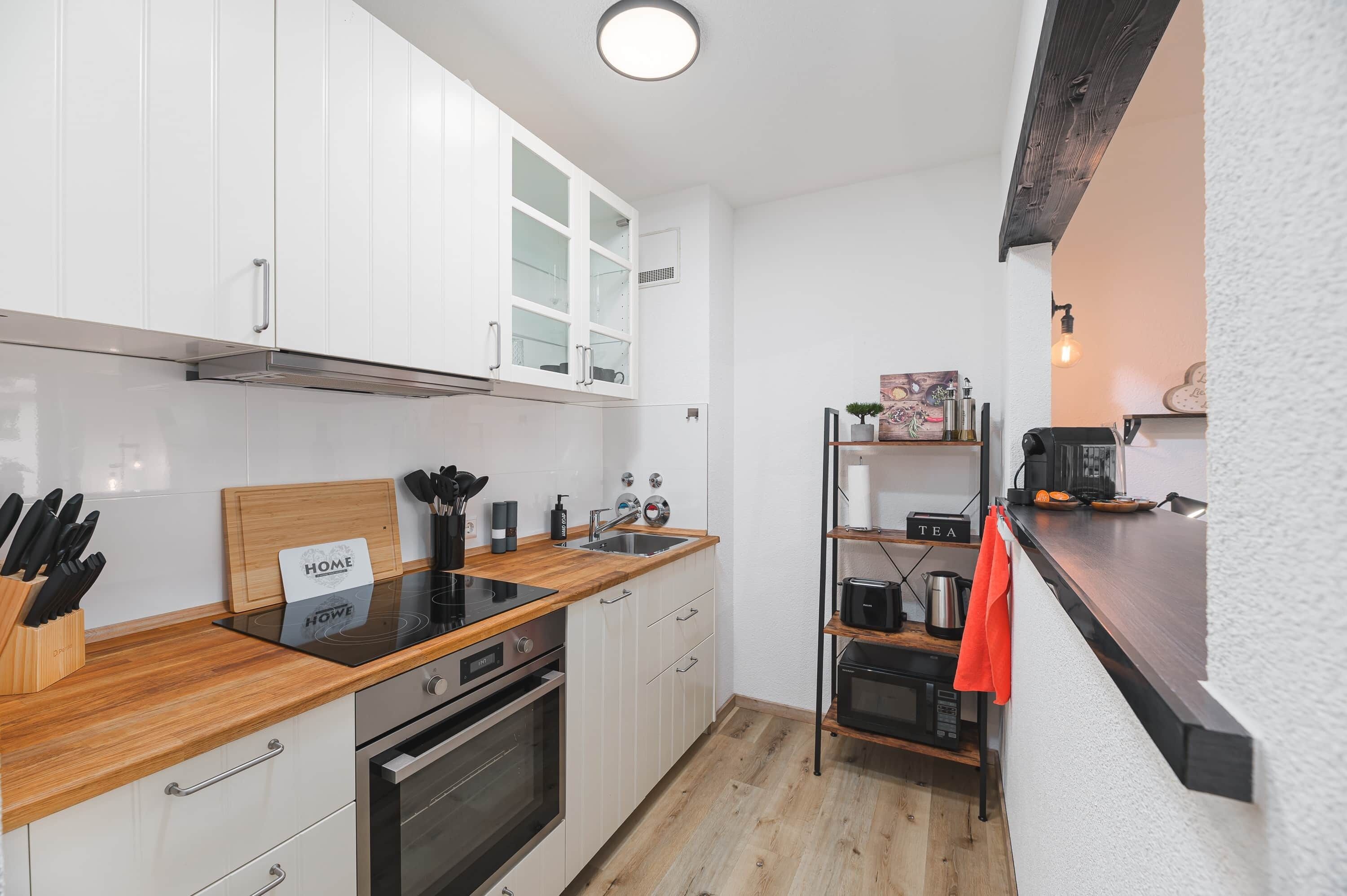 Een moderne keuken met witte kastjes, een houten aanrecht en roestvrijstalen apparatuur.