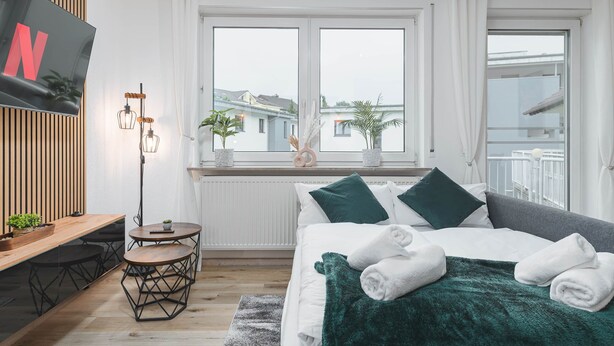 Ein modernes Hotelzimmer mit einem großen Bett, einem Schreibtisch mit Stuhl, einem kleinen runden Tisch und einem an der Wand befestigten Fernseher.