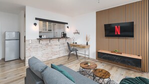 Ein modernes Wohnzimmer mit einem grauen Sofa, einem Holztisch und einem an einer Holzwand montierten Fernseher.