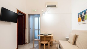 A small, well-lit room with a wooden dining table, four chairs, a beige sofa, a flat-screen TV mounted on the wall, and a painting on the wall. - Meta Apartment by Wonderful Italy  (Bari)