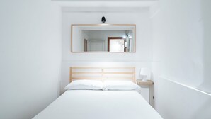 A minimalist hotel room with a single bed, a nightstand, a bedside lamp, and a mirror above the bed. - Meta Apartment by Wonderful Italy  (Bari)