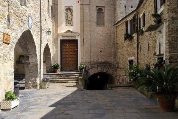Une cour pavée de pierres, avec une porte centrale, des passages en arc de cercle et une petite cheminée.