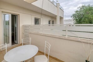 A balcony with a white table and chairs, a sliding glass door, and a view of a building and tree.