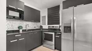 Une cuisine moderne avec des meubles de rangement aux couleurs sombres, un réfrigérateur en acier inoxydable, un four à micro-ondes et un four traditionnel.
