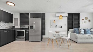 Une cuisine moderne avec des meubles de couleur sombre, des appareils en acier inoxydable et un coin repas comprenant une table et des chaises blanches.