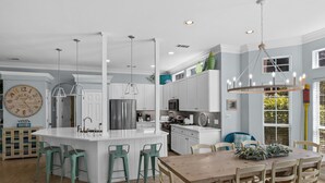 Una cocina moderna con armarios blancos, una isla central con taburetes y una zona de comedor con sillas de madera.