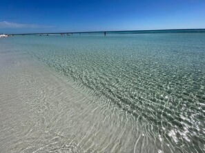 Una playa con aguas transparentes y poco profundas, una orilla de arena y un horizonte lejano.