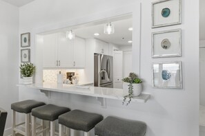 Una cocina moderna con armarios blancos, un refrigerador de acero inoxidable y una zona de bar con taburetes.