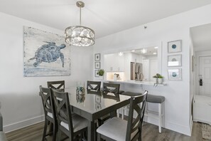 Un comedor con una mesa de vidrio, sillas de madera oscura, una lámpara colgante y un cuadro grande de una tortuga en la pared.