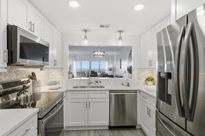 Una cocina moderna con armarios blancos, electrodomésticos de acero inoxidable, lavavajillas y un refrigerador grande.