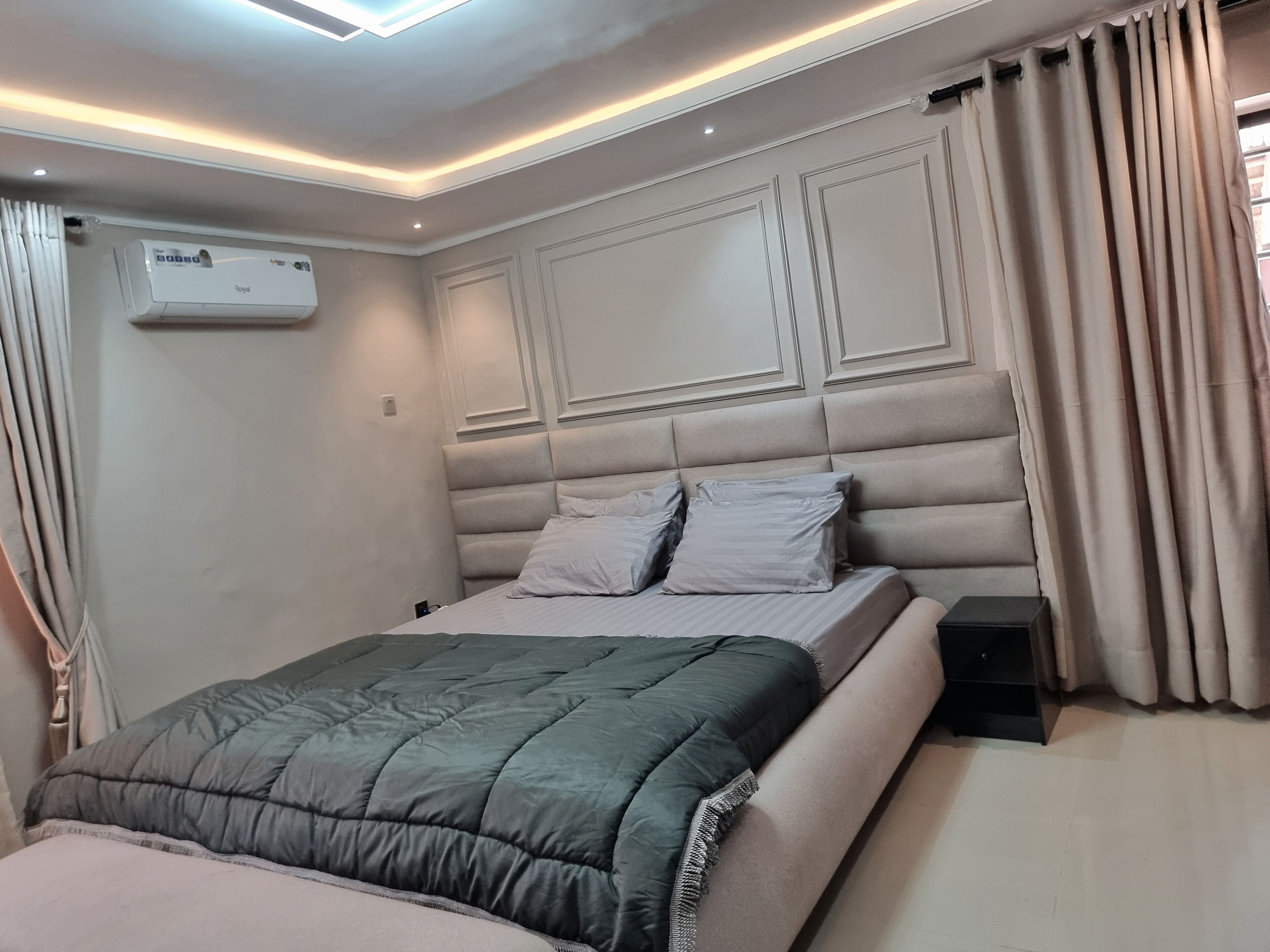 Une chambre à coucher moderne avec un grand lit, une tête de lit intégrée et un appareil de climatisation fixé au mur.