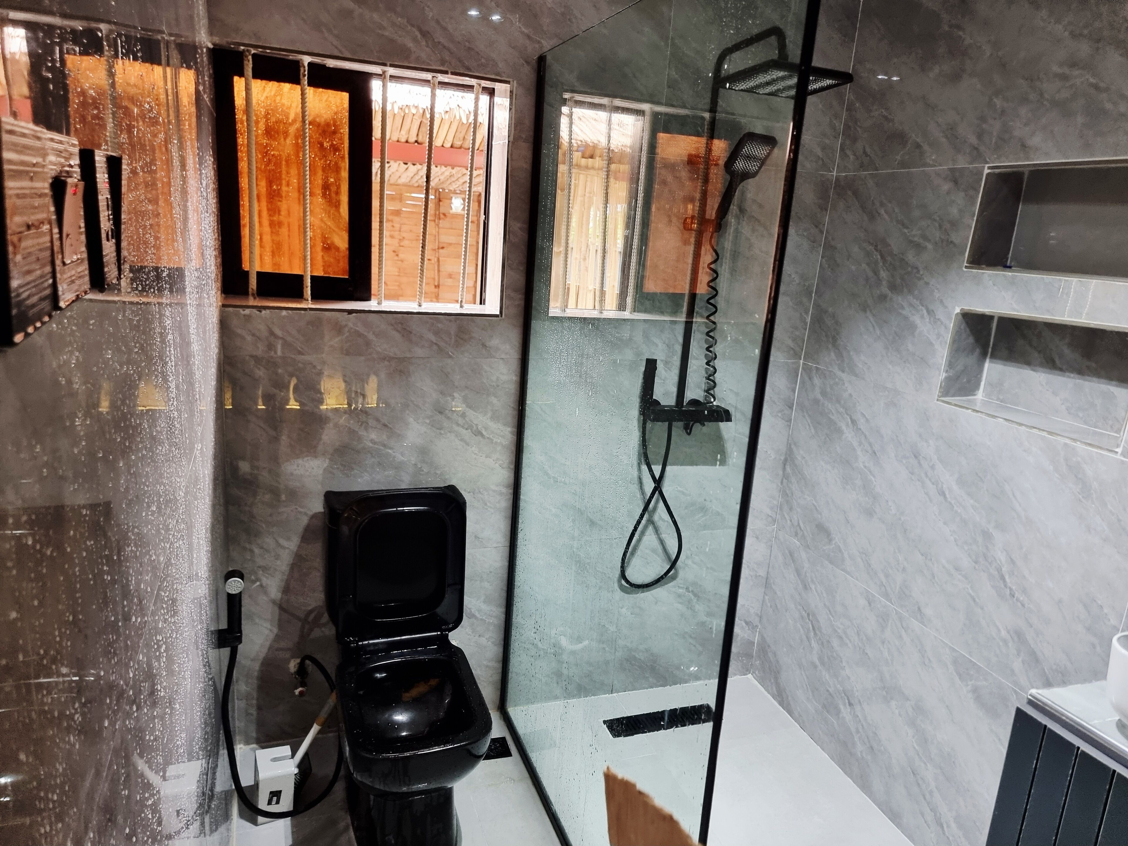A modern bathroom with a glass-enclosed shower, a black toilet, and a marble-tiled wall.