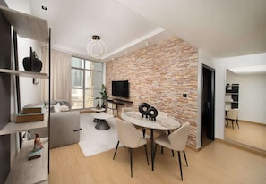 A modern living room with a stone wall, a round dining table, and a TV mounted on the wall. - Dubai Marina Apt w/ Pool, Gym & Balcony Views (Dubai)