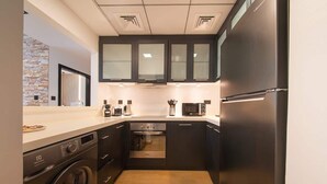 A compact kitchen with a washing machine, a microwave, and a refrigerator. - Dubai Marina Apt w/ Pool, Gym & Balcony Views (Dubai)