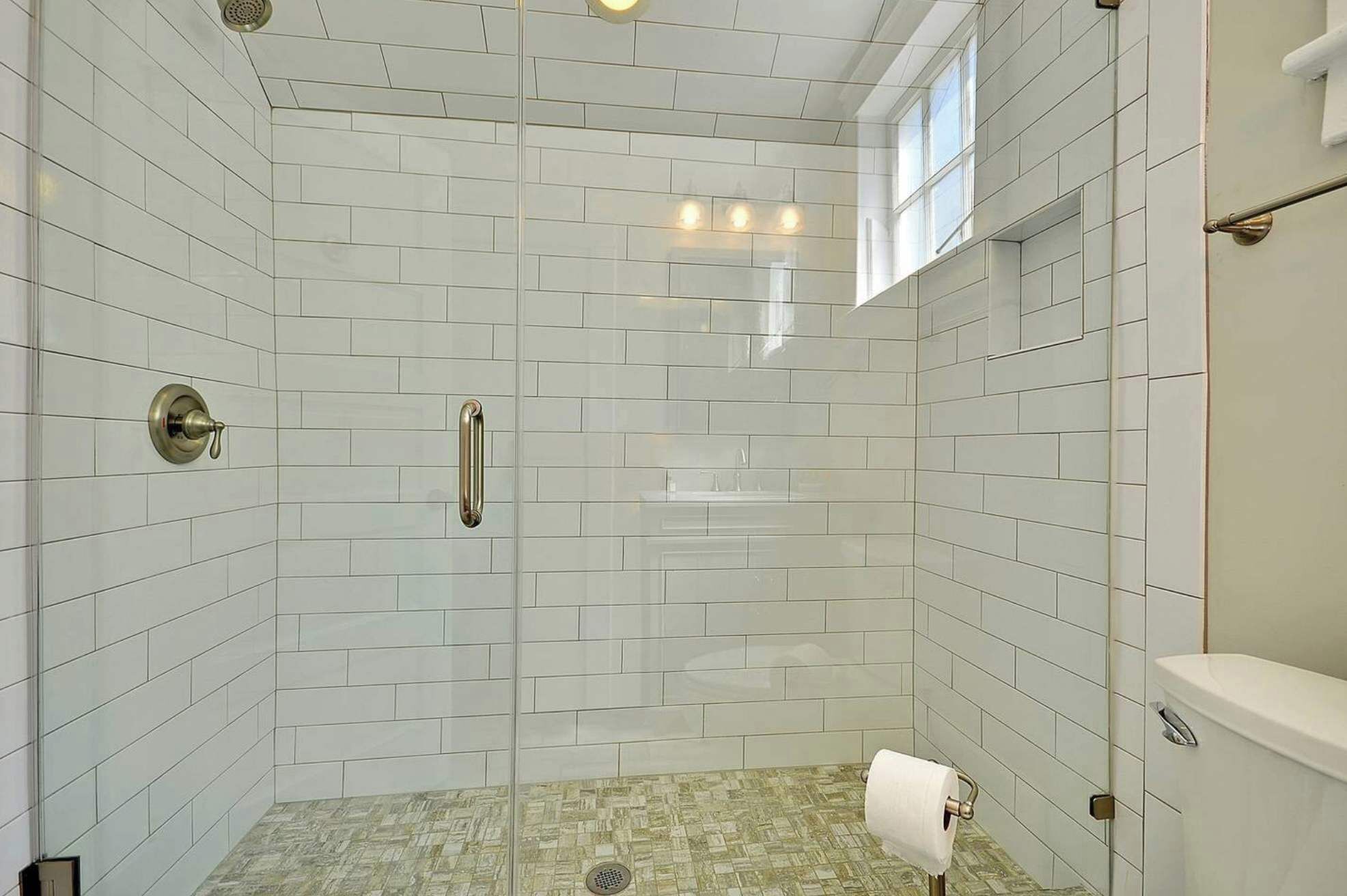 A walk-in shower with white subway tiles, a glass door, a towel rack, and a toilet paper holder.
