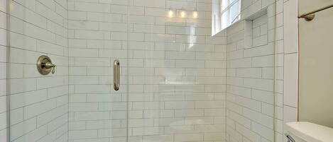 A walk-in shower with white subway tiles, a glass door, a towel rack, and a toilet paper holder.