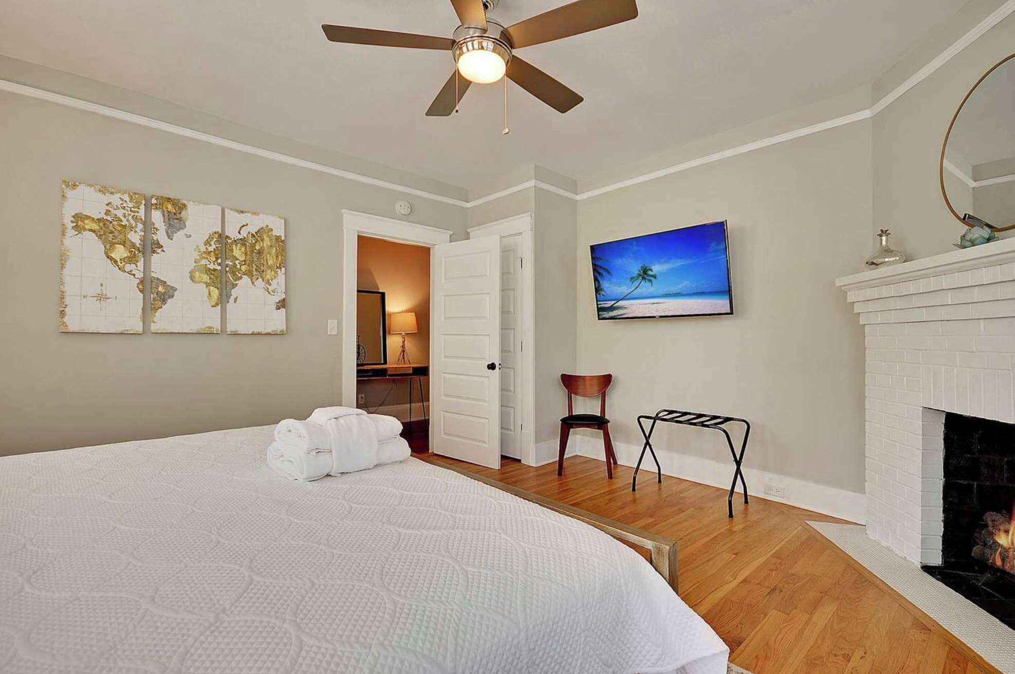 A bedroom with a bed, a ceiling fan, a painting of a beach, a fireplace, and a map on the wall.